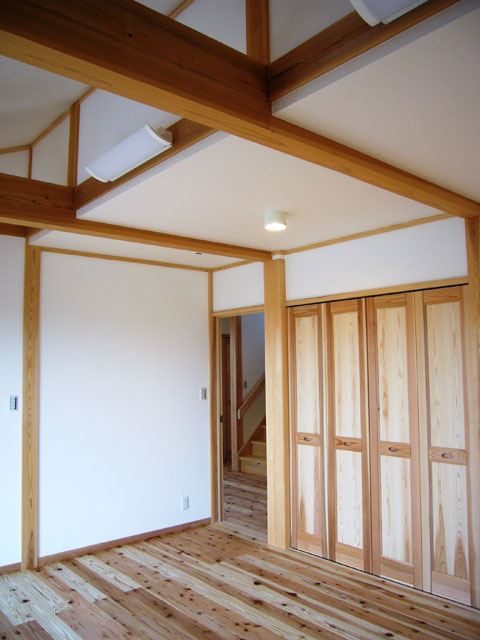 同じく２階の寝室。一部勾配なりの天井。杉の大きな平角を使って圧迫感を減少。クローゼットの扉はムクの杉材の建具。