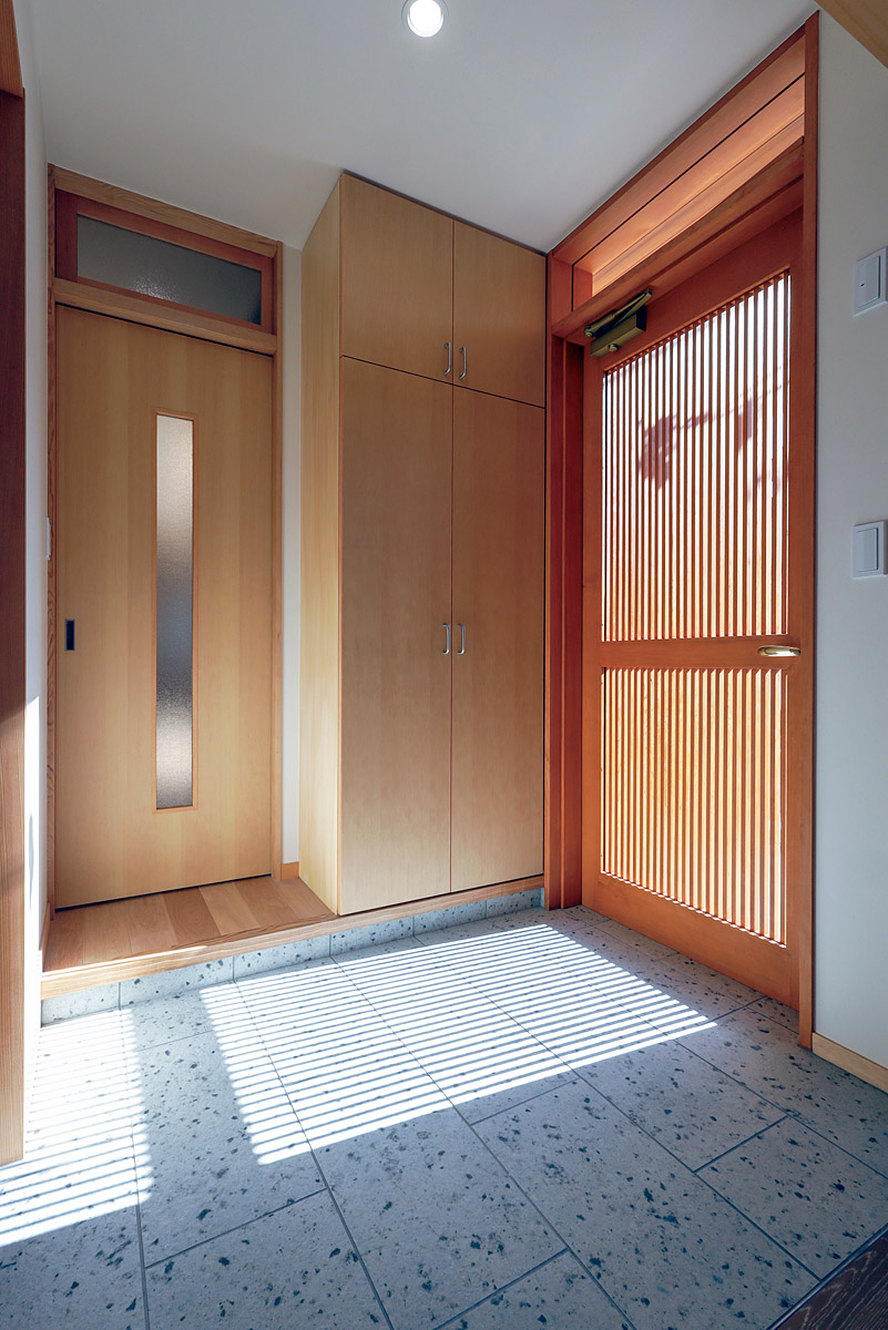 玄関床は大谷石調のタイル貼り、玄関扉は細かい縦桟の木製扉にしています